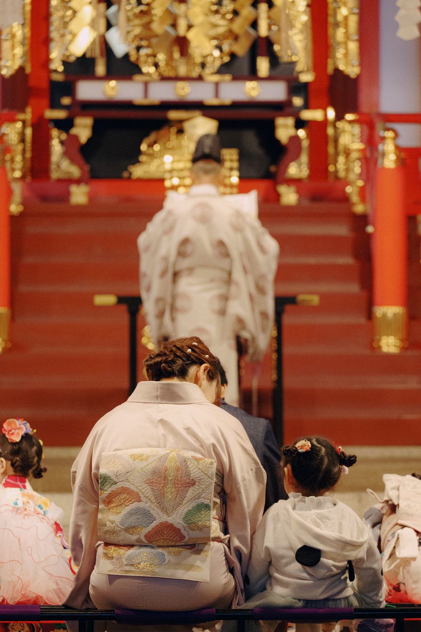 晴れ着姿の子供と家族が神社の社殿で祈祷を受ける様子。七五三のイメージ写真
